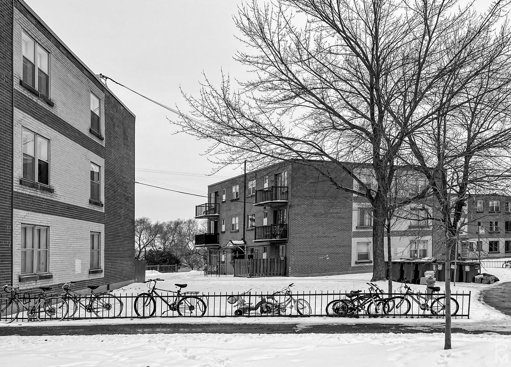 Digital image of the yard in front of apartment buildings in winter with a row of bikes along a fence