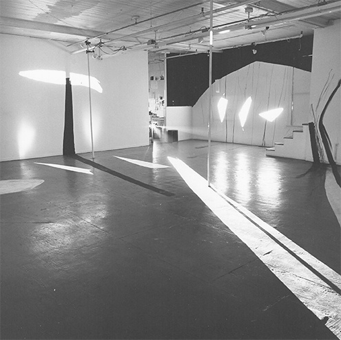 Black and white view of ART PLAY II installation with painting on the gallery walls, floor and ceiling and geometric light projections across the gallery floor.