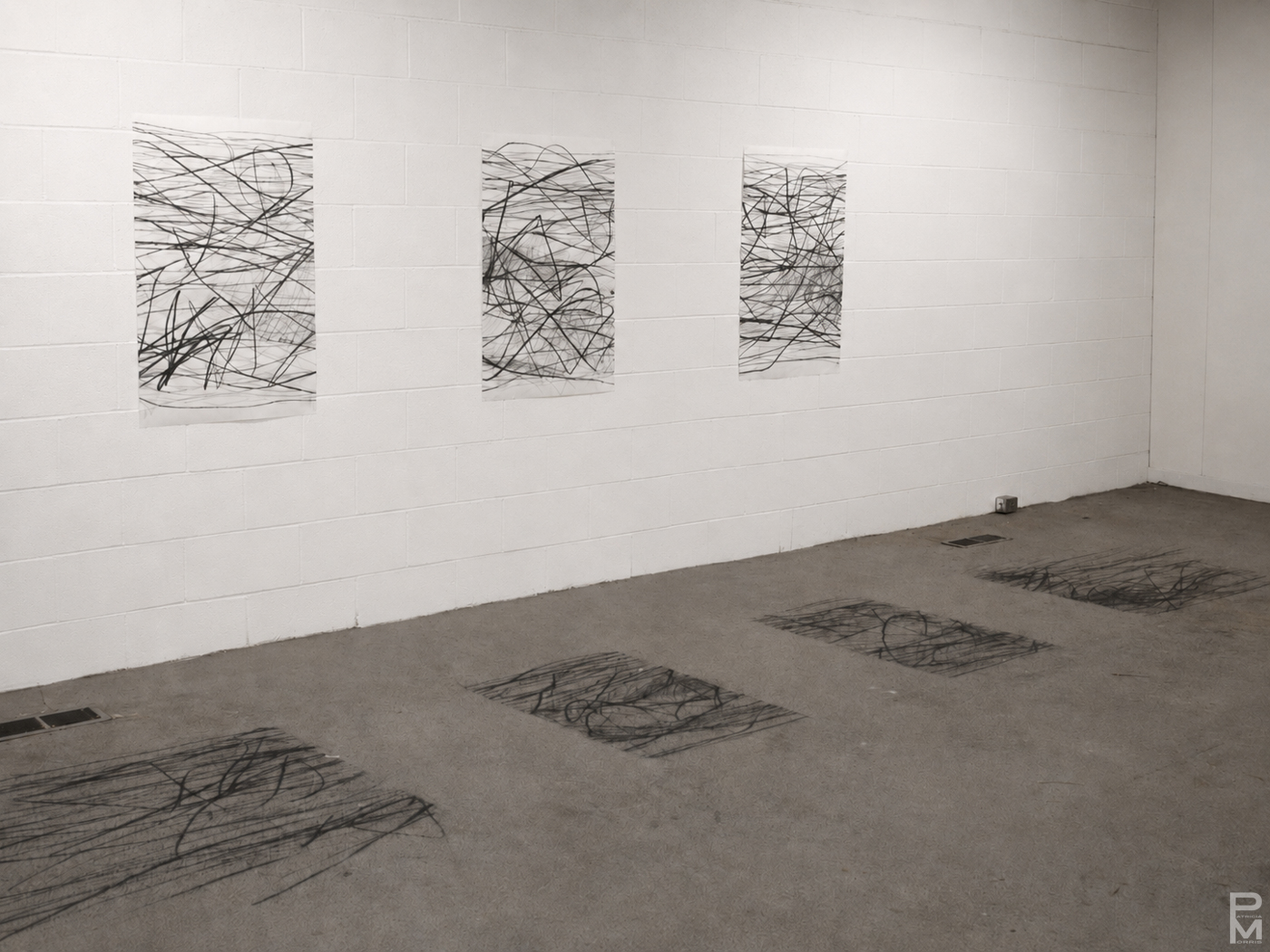 Photograph of installation where three panels of an abstract drawing on the floor have been removed and placed on the wall beside it.