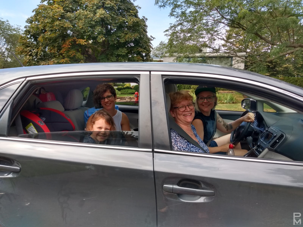 Family piled into a car, smiling out the windows before setting off on a road trip
