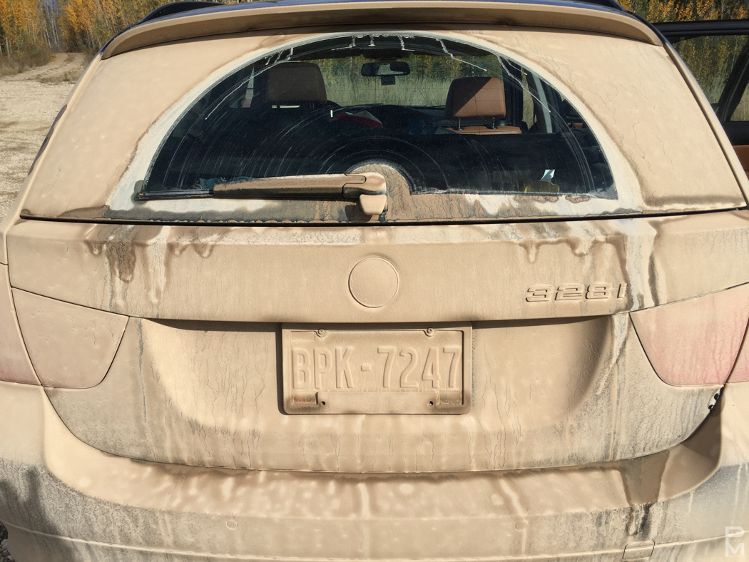 Back of a car completely coated in dried mud from a gravel road
