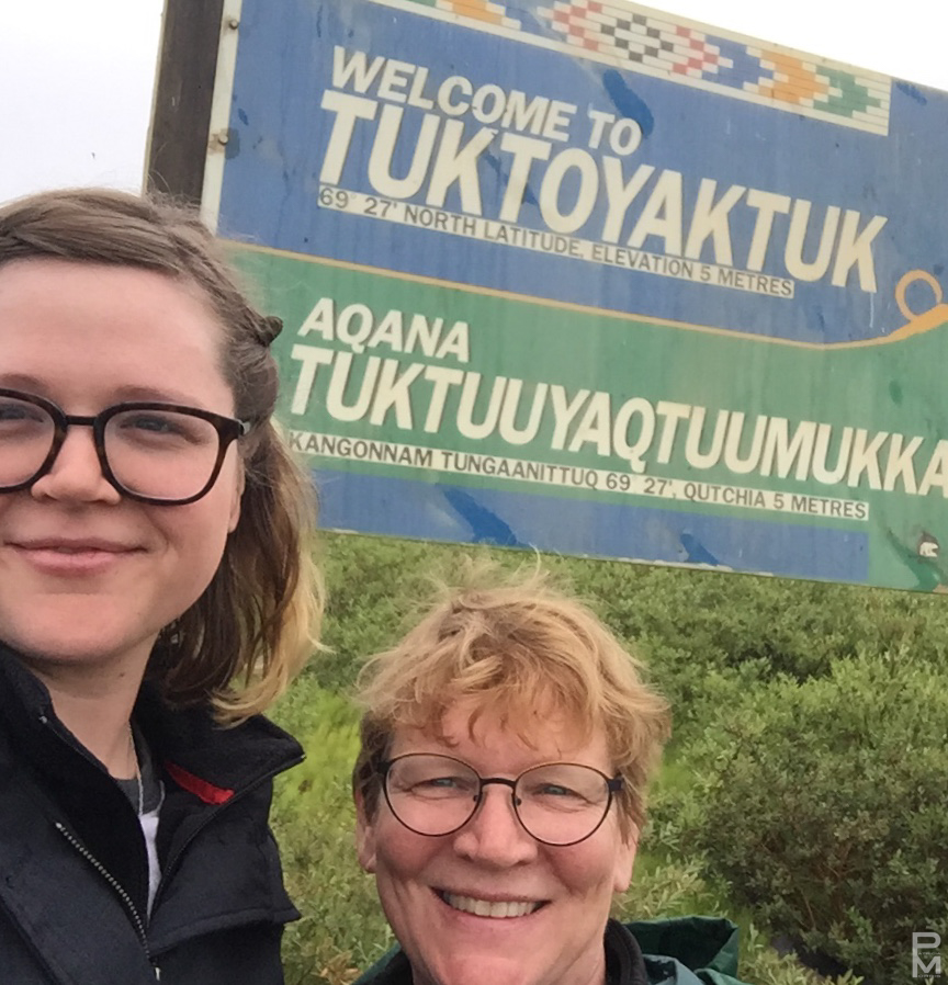 Two people posing in front of the Welcome to Tuktoyaktuk sign