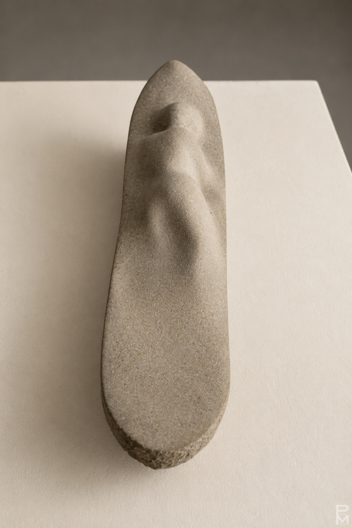 Sandstone sculpture of a long low boat with the shape of a figure melting into the boat.